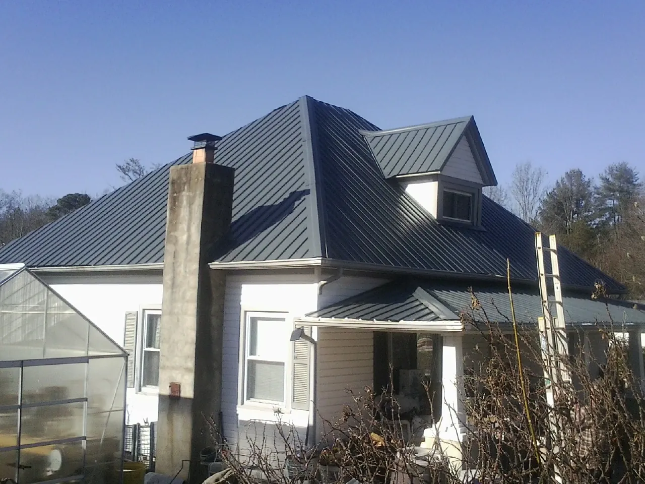 Dark blue standing seam metal roof on a white farmhouse with dormer in Belleville